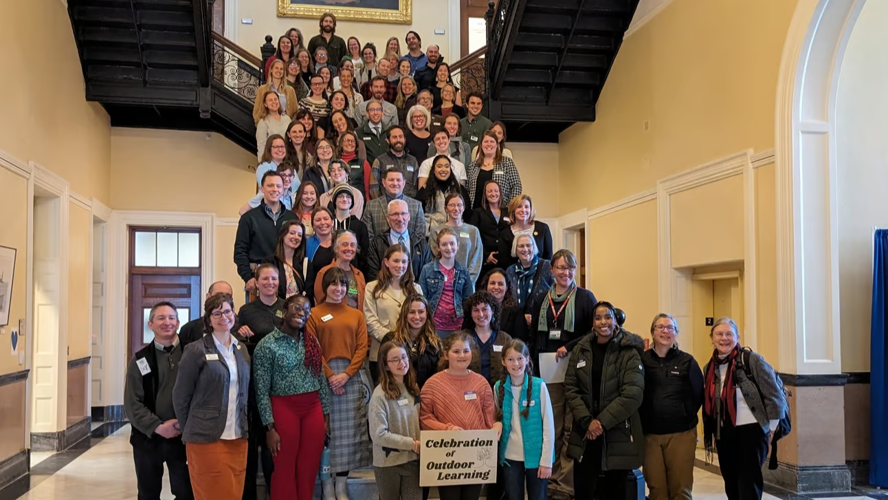 A large group of outdoor education advocates pose for a photo while standing on a staircase at the Maine State House.