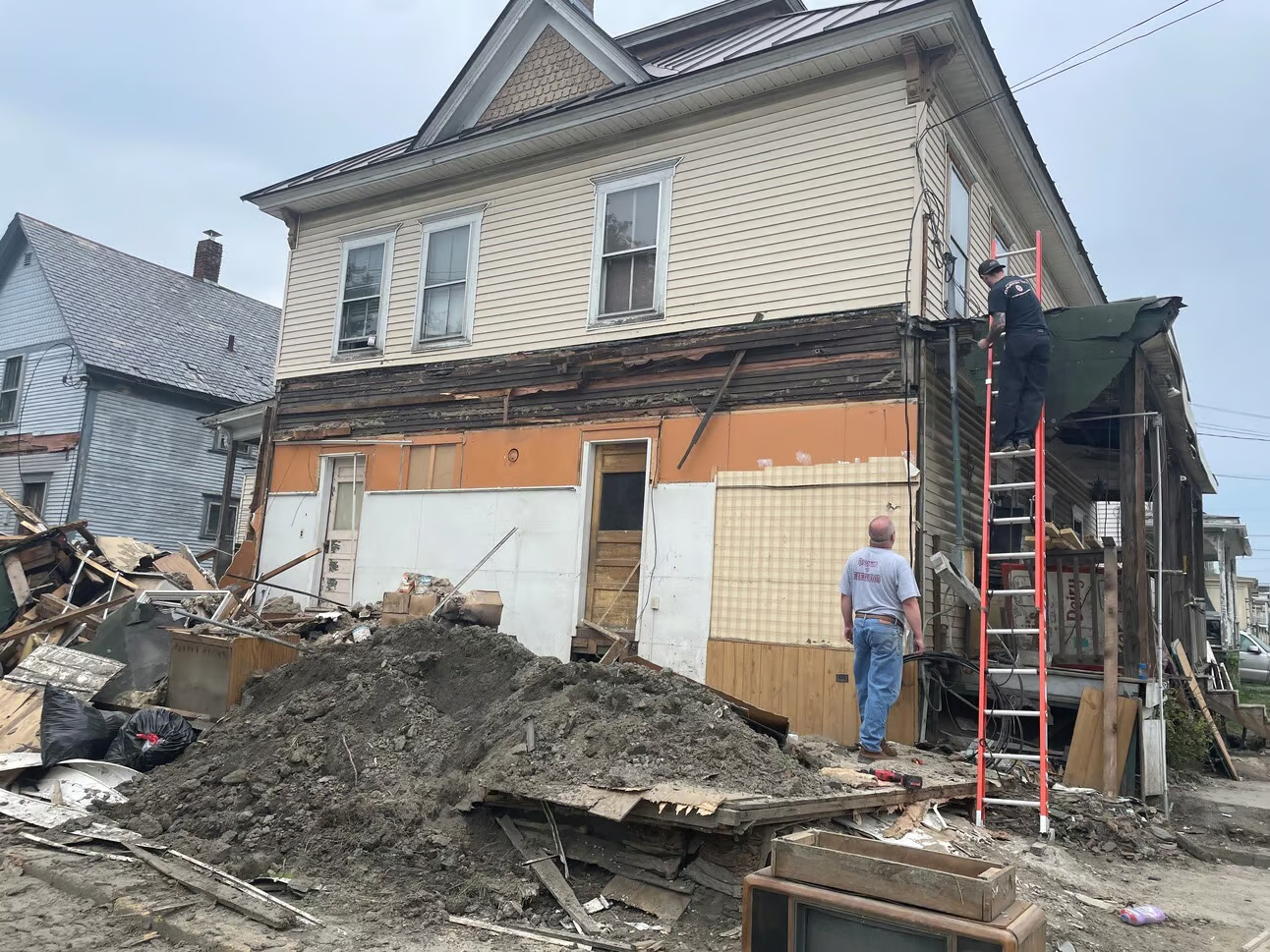 Workers outside the home, including one climbing a ladder and one supervising.