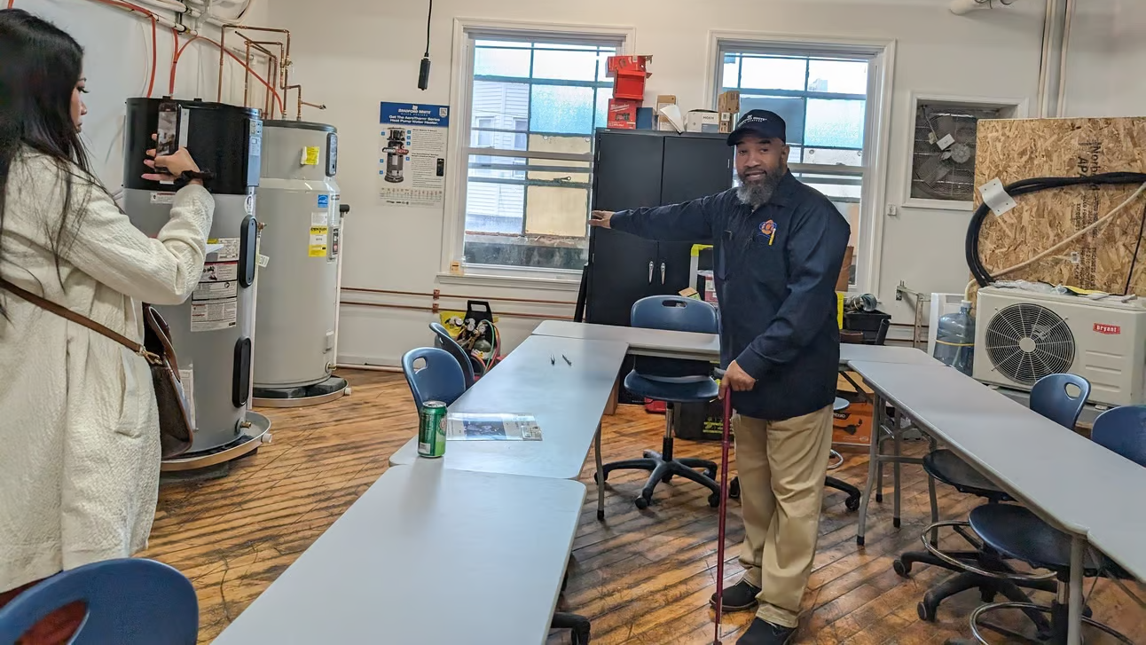 A man points to a heat pump system while conducting a facility tour.