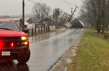 An emergency vehicle blocks the road where a downed utility pole is nearly falling into the roadway.