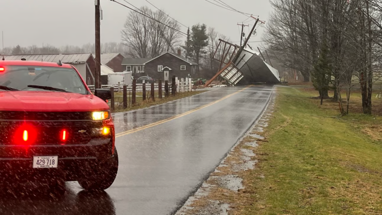 An emergency vehicle blocks the road where a downed utility pole is nearly falling into the roadway.