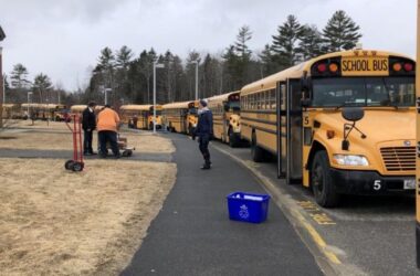 School buses lined up at the curb of a school in Maine.