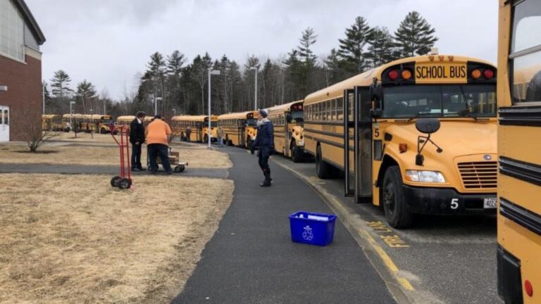 School buses lined up at the curb of a school in Maine.