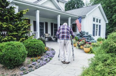 A man uses a walker to get up the walkway to his home's front door.