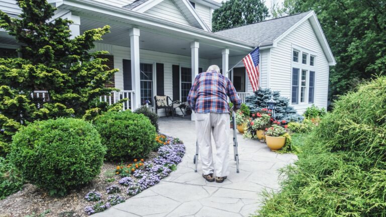 A man uses a walker to get up the walkway to his home's front door.