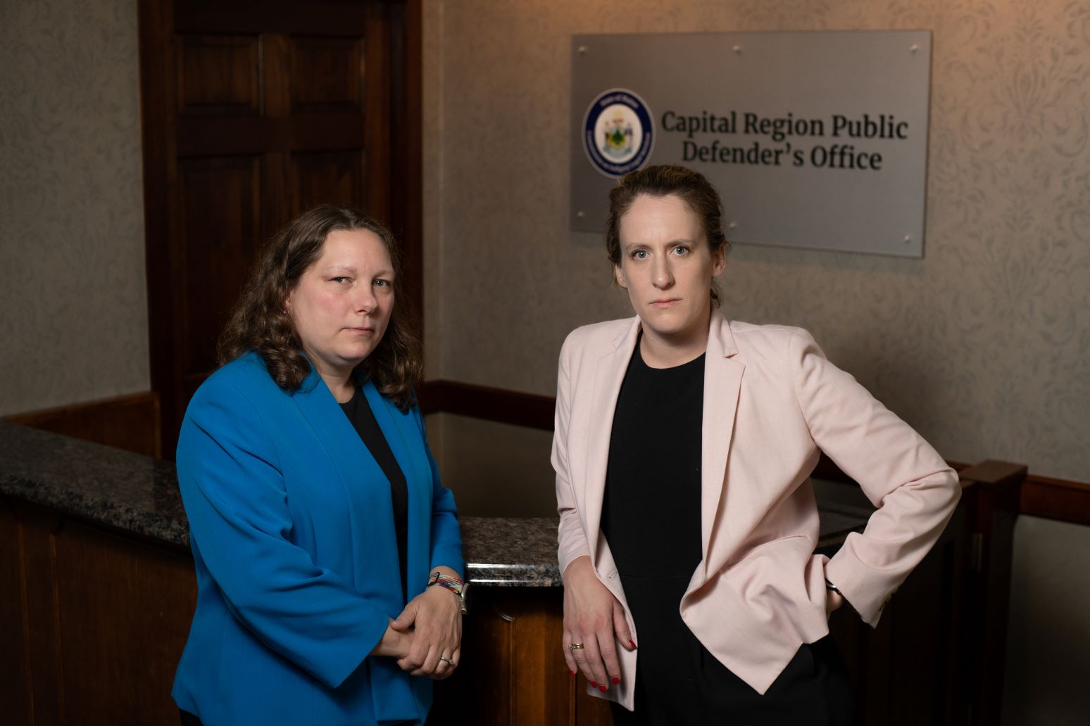 Frayla Tarpinian and Hillary Knight pose for a photo in front of a sign for the public defender's office.