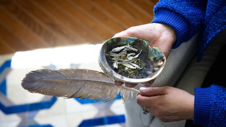 Two hands hold an abalone shell and an eagle feather.