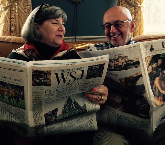 Naomi Schalit and John Christie pose for a photo while holding a newspaper.