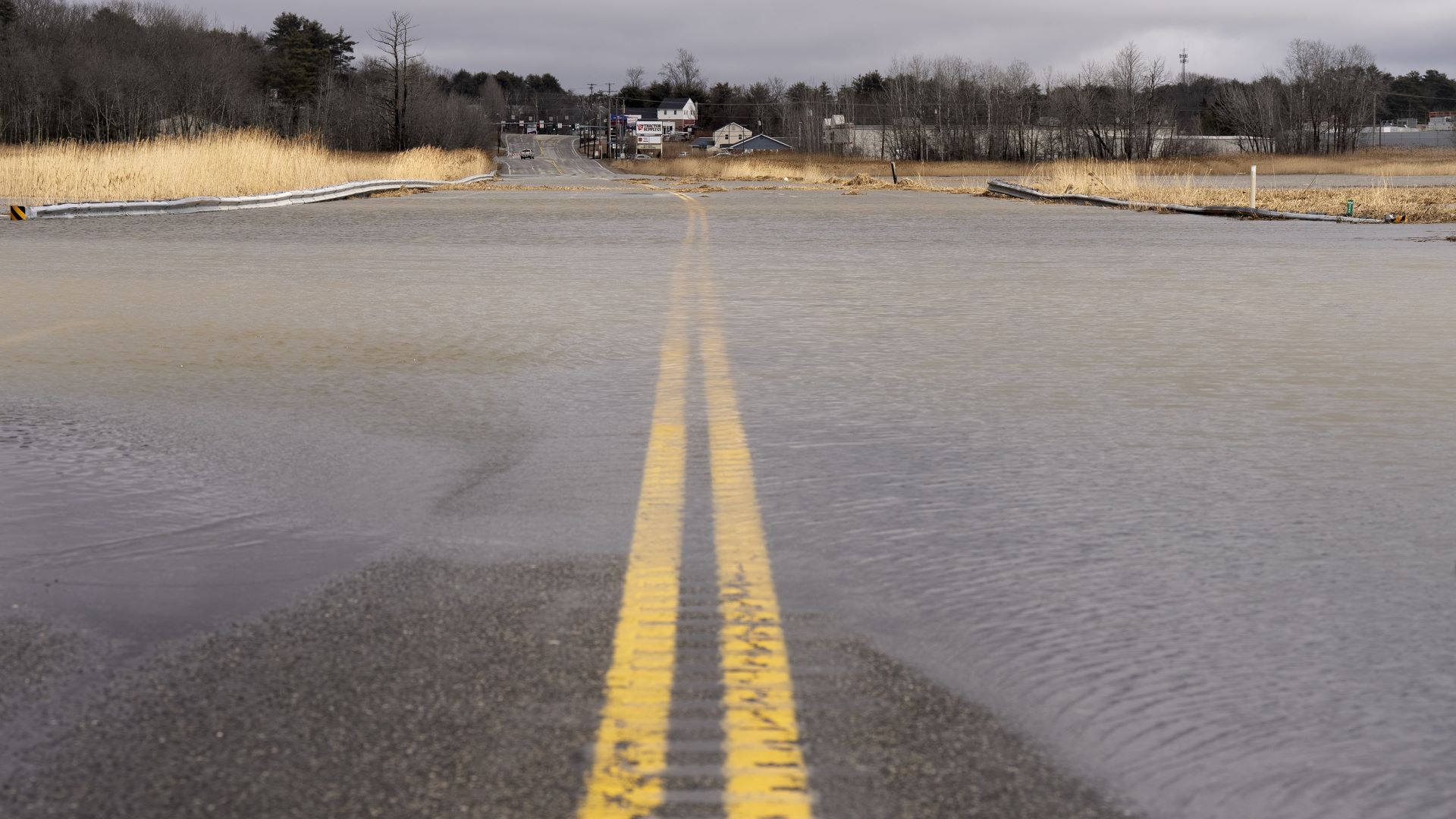 A flooded roadway with residential homes in the distance.