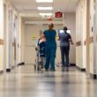 nurses walking down a hallway while pushing a patient in a wheelchair.