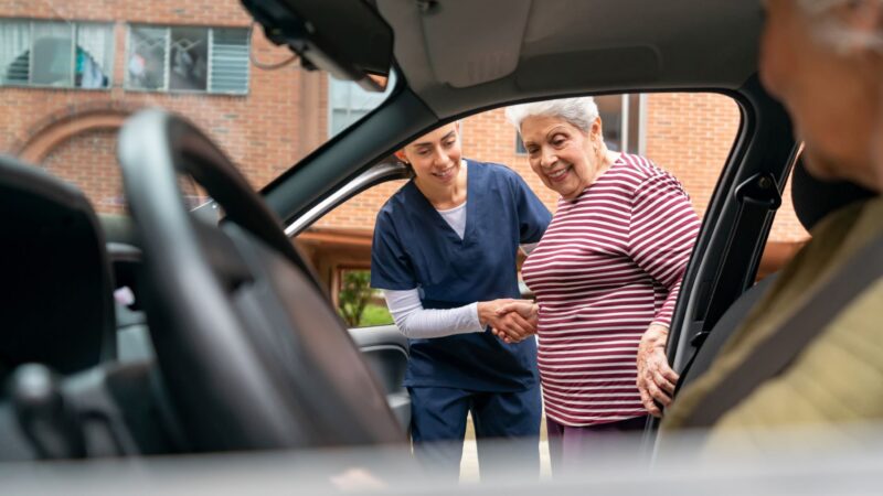 A health aide assists a woman as she gets inside a personal medical transport vehicle.