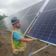 A man installs solar panels in a field.