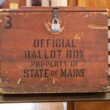 A locked wooden box stamped with the phrase "Official ballot box property state of Maine"