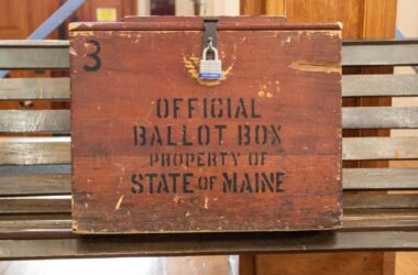 A locked wooden box stamped with the phrase "Official ballot box property state of Maine"