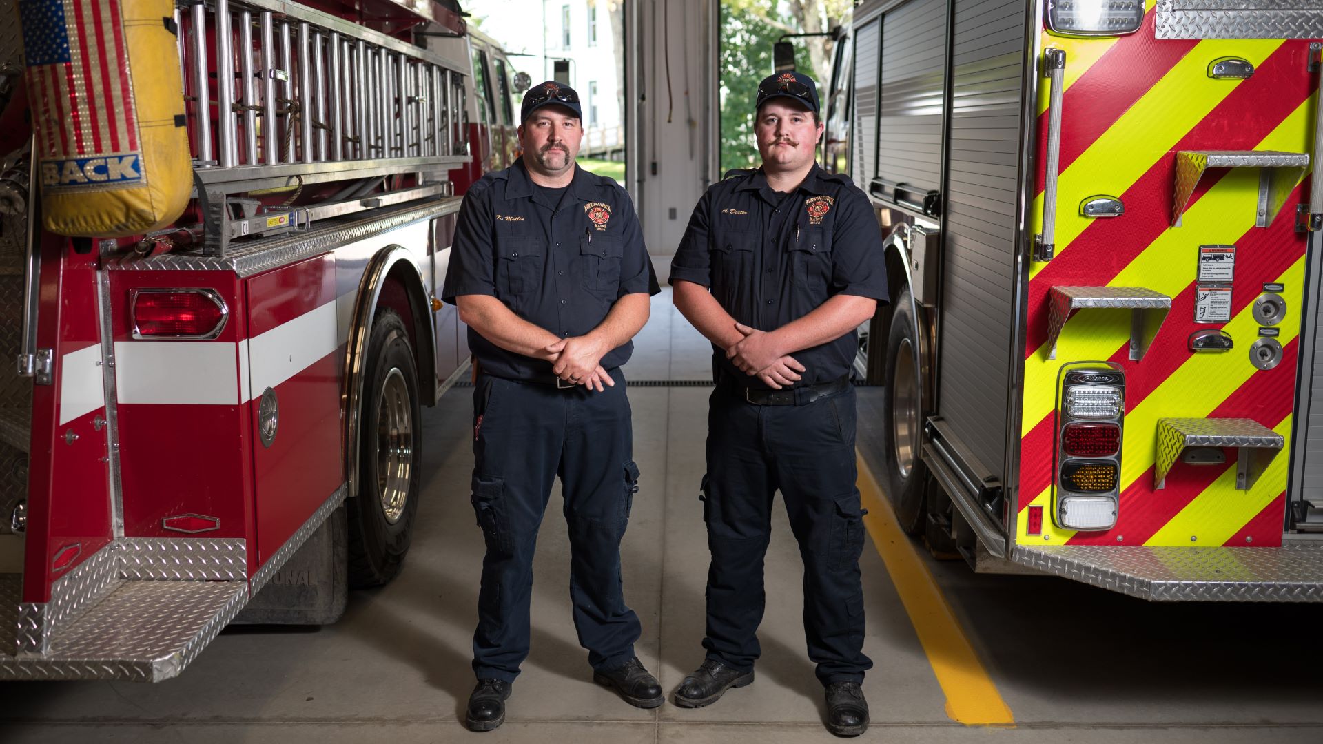 Kyle Mullin and Andrew Dexter pose for a photo while standing between two fire trucks.