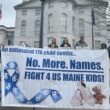 People attending a rally hold a large banner that reads "An estimated 178 child deaths. No more names. Fight for us Maine kids."