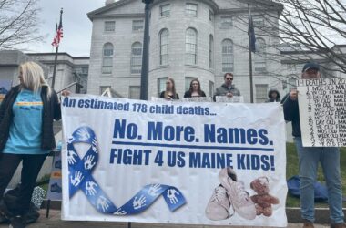 People attending a rally hold a large banner that reads "An estimated 178 child deaths. No more names. Fight for us Maine kids."