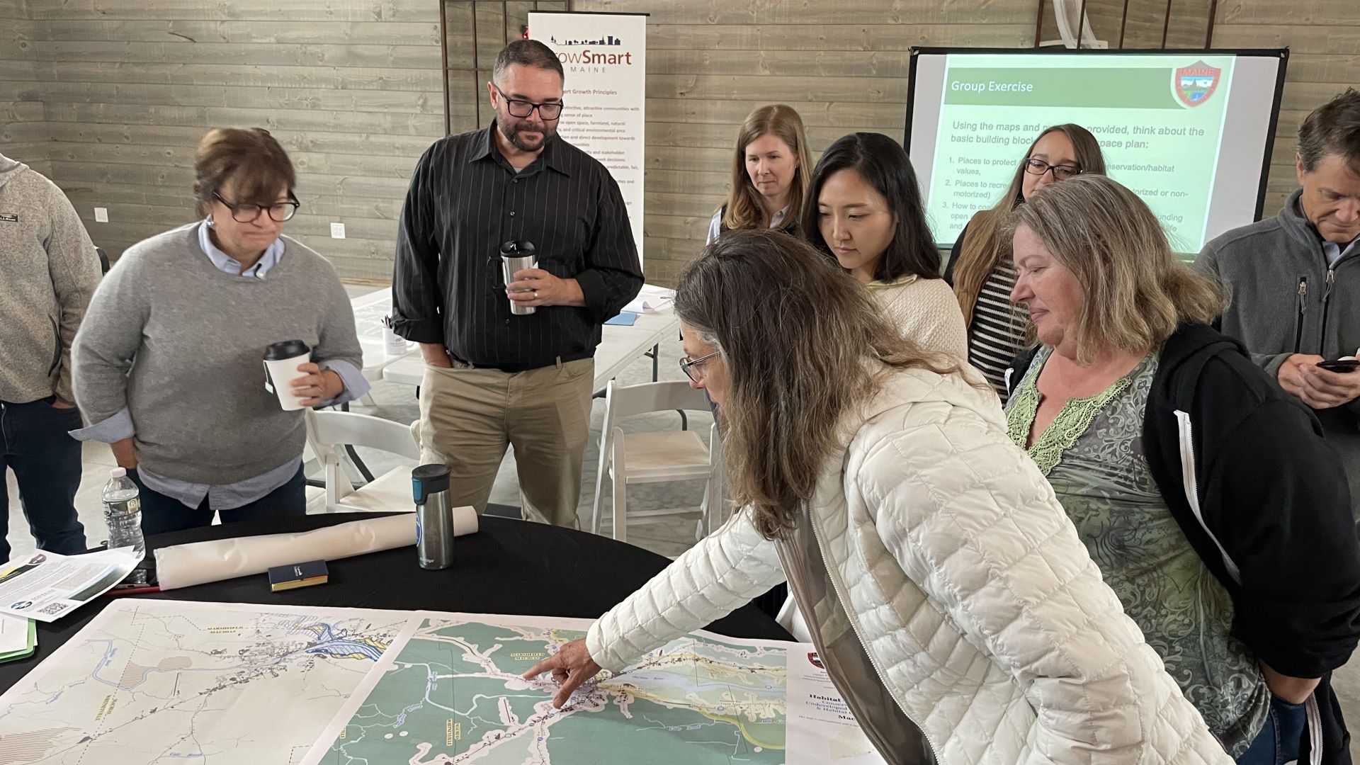 Individuals gathered around a table that has a large map on top of the table.