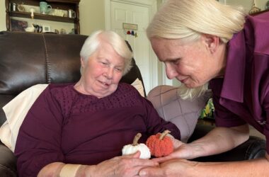 A personal care aide interacts with a client that is holding small knitted pumpkins.