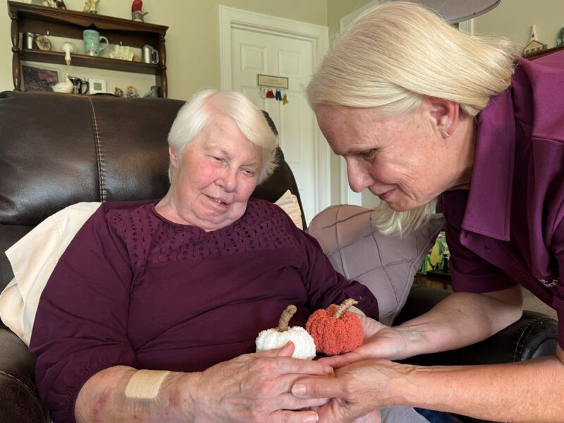 A personal care aide interacts with a client that is holding small knitted pumpkins.