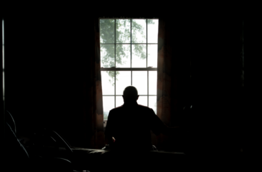 a silhouette image of a nursing home resident looking out a window.