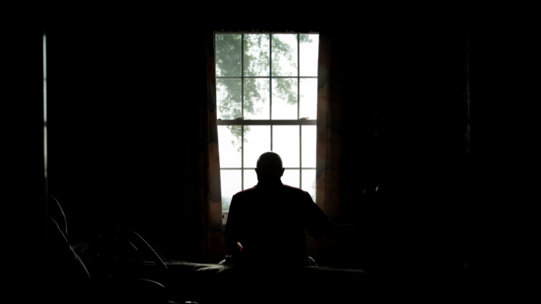 a silhouette image of a nursing home resident looking out a window.