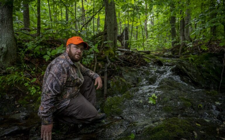 brandon bishop poses for a photo in the woods.
