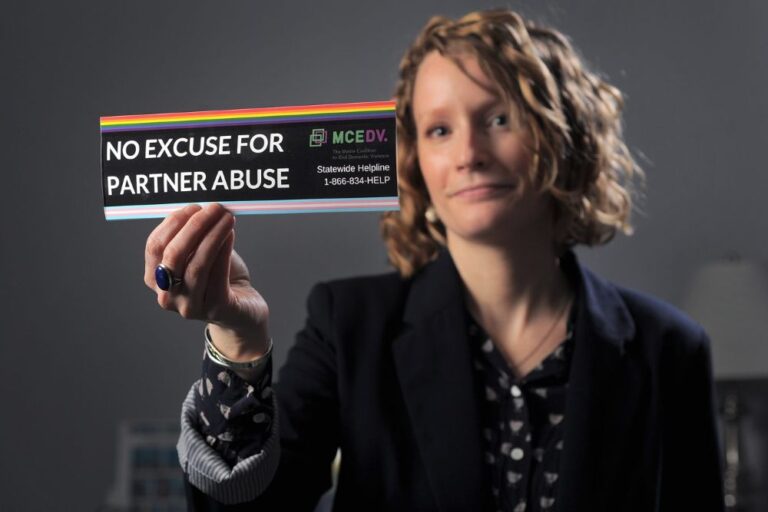 a woman holds a bumper sticker that reads no excuse for partner abuse.