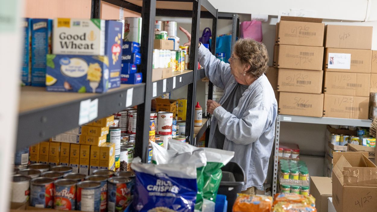 A woman reaches toward an item on a food pantry shelf.