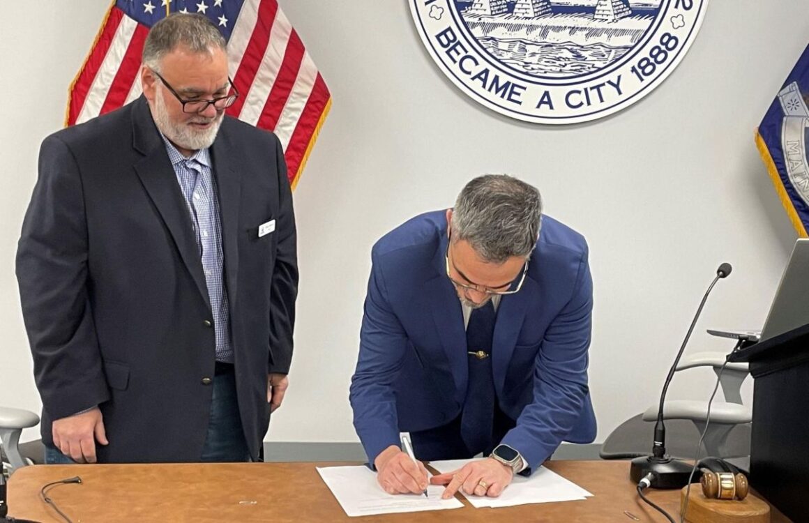 Nick Cloutier signs his contract while the mayor stands nearby.