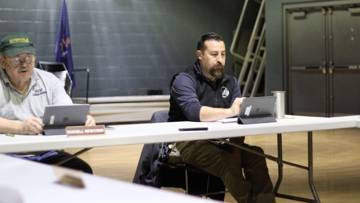 two men sitting at a table during a select board meeting.