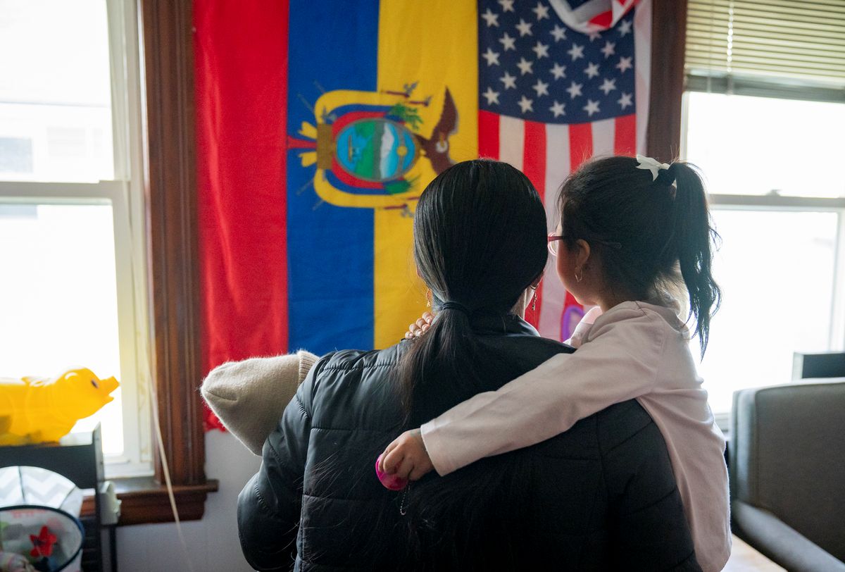 Maria holds her young daughter while looking at flags of Ecuador and the U.S.