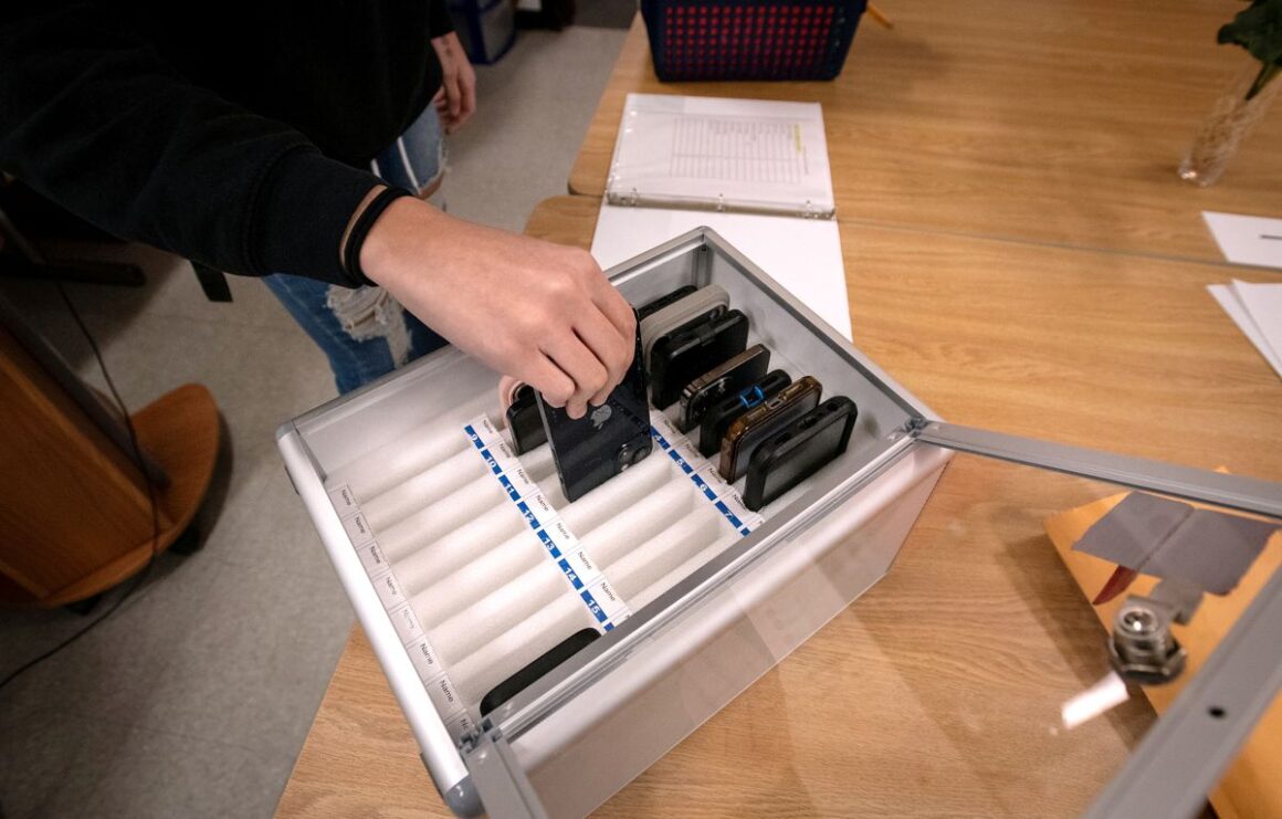 student puts their cell phone in a metal box that sits on a table.