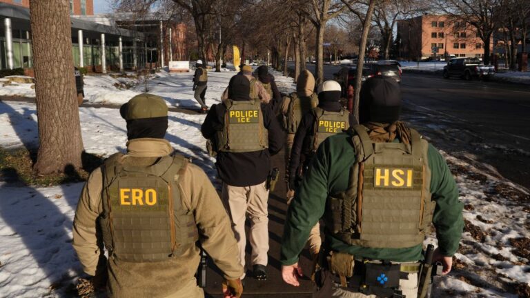 Federal law enforcement agents walk through a neighborhood.