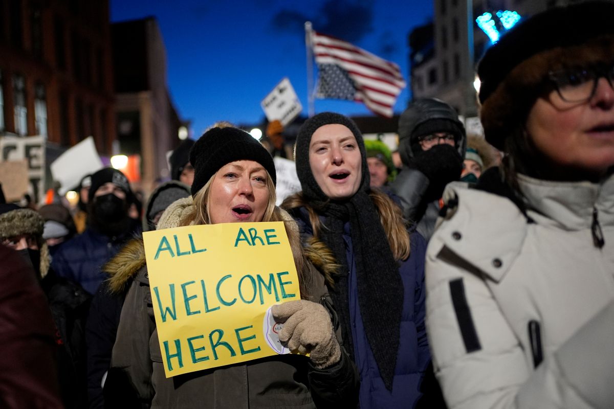 a protester holds a sign that reads all are welcome here.