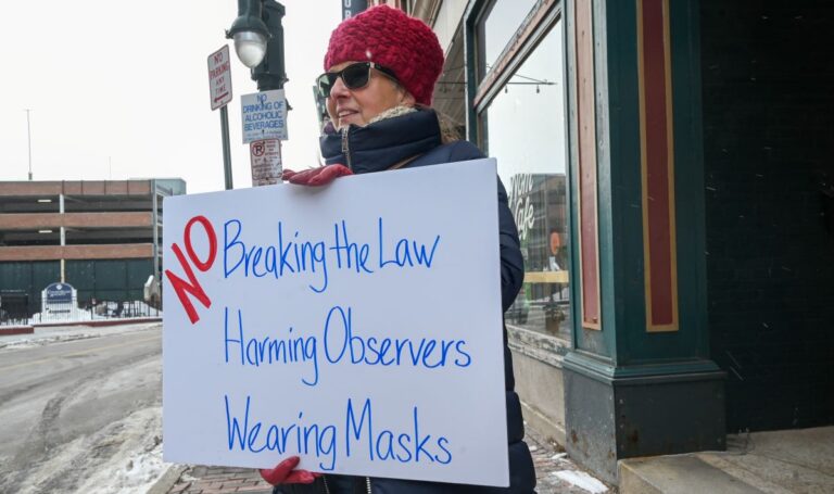 woman holding a sign that reads no breaking the law, harming observers, wearing masks.
