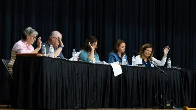members of the RSU 39 school board raise their hands during a vote.
