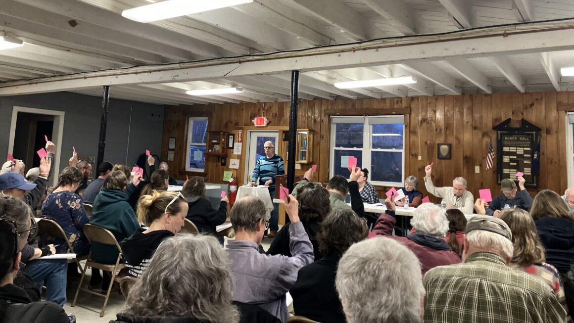 Voters raise pink sticky notes to cast their vote.
