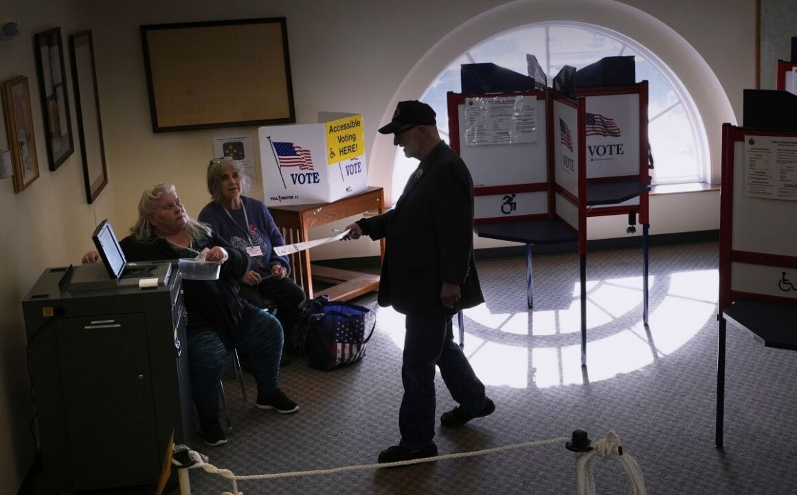 a voter prepares to put their ballot in a tabulation machine.