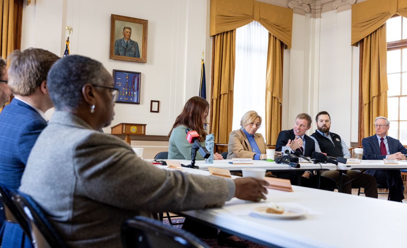 Government officials from Maine sit around tables during a press conference.