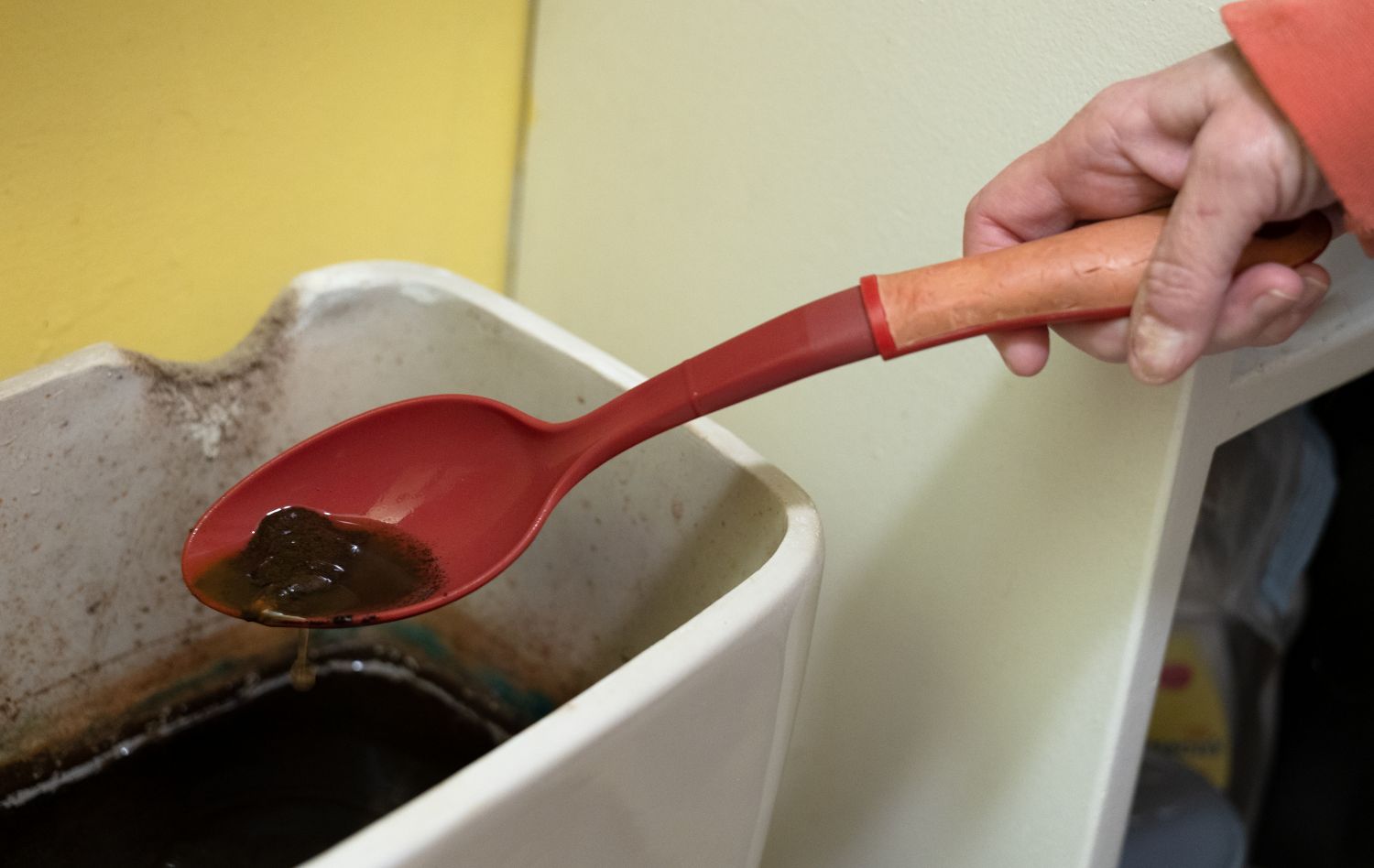 a resident uses a large red spoon to show the dirty water in their toilet tank