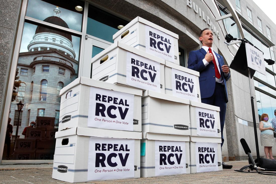 Jason Savage stands next to stacked boxes that have "Repeal RCV" on the side of the boxes.