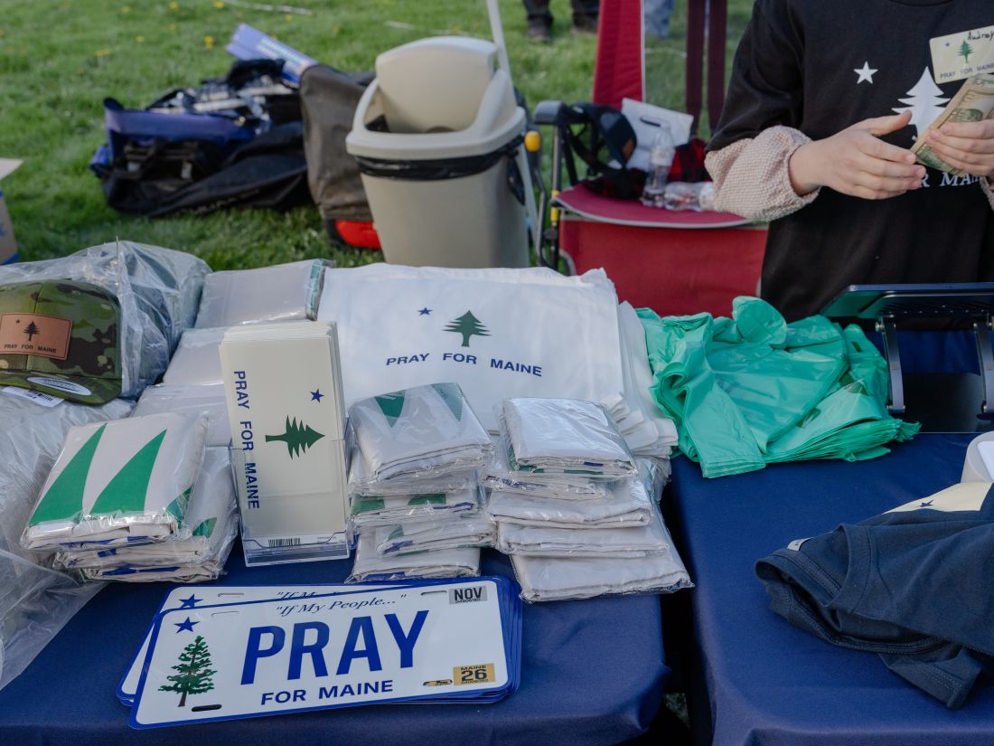 a merch table with Pray for Maine branded bags, shirts and hats.