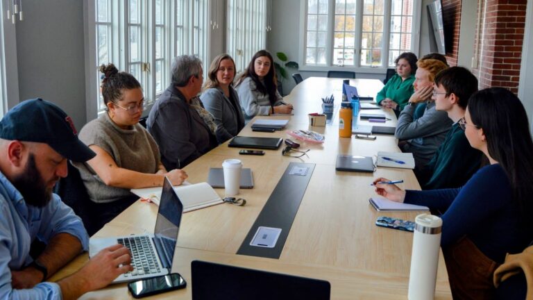 members of The Maine Monitor gather around a conference room table during a staff meeting.