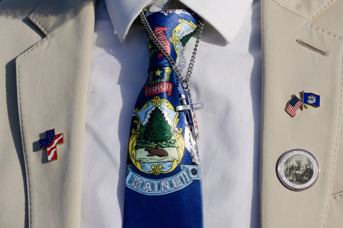 a man wearing a state of maine tie and a cross necklace
