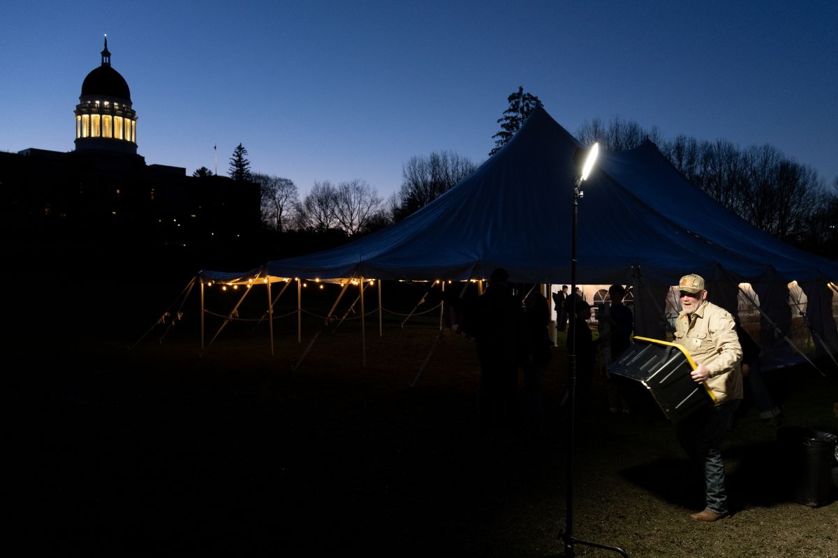 a man carries a container with the lit dome of the state house visible in the background.