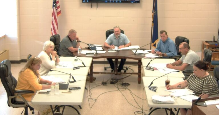 Members of the council sit around tables during a meeting.