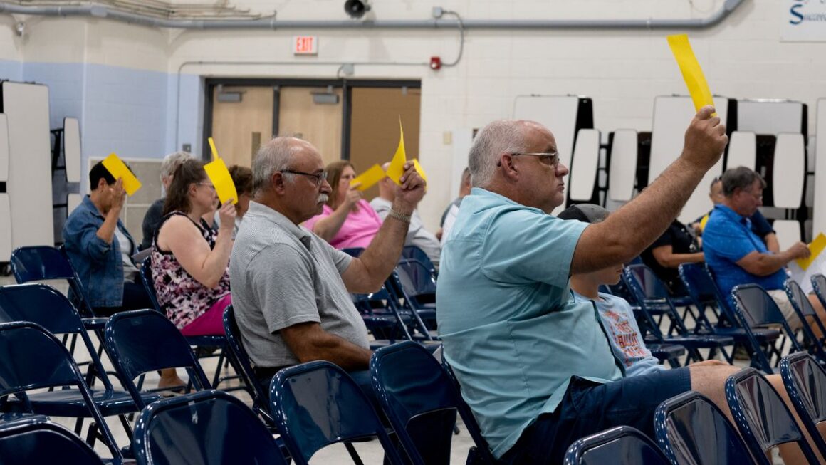 people in a crowd hold up gold voting cards.