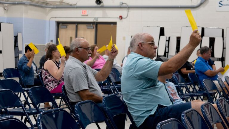 people in a crowd hold up gold voting cards.