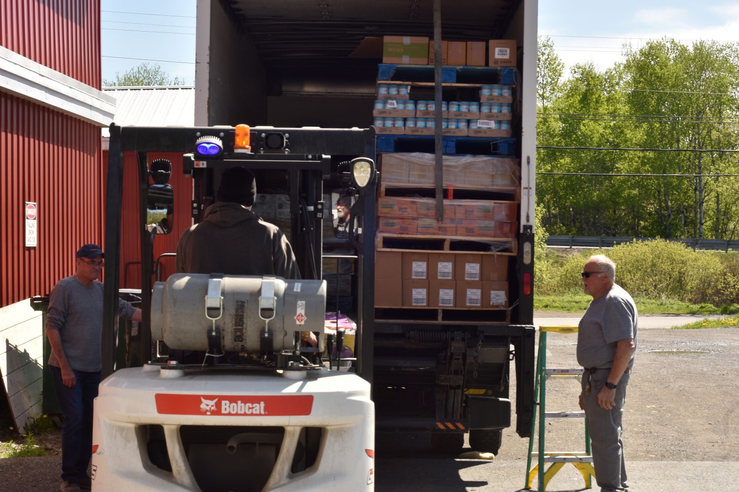 Two men watch as a pallet is loaded into a box truck.